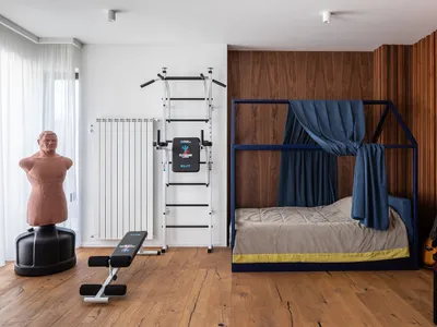 A minimalist bedroom with a blue canopy bed, wooden walls, and exercise equipment.