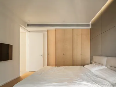 Modern minimalist bedroom featuring wooden cabinets and a white bed.
