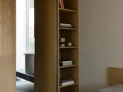 A minimalist bedroom with a wooden bed and built-in shelves against a white brick wall.