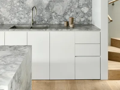 A minimalist kitchen with white cabinets and marble countertops.