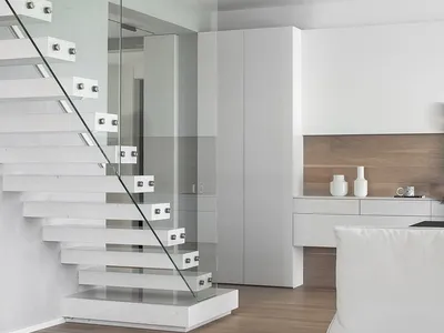 A minimalist apartment living room featuring a white staircase with glass railings, wooden flooring, and white furniture.