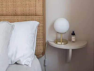 Minimalist bedroom with a woven bed frame and a wall-mounted nightstand with a spherical light and essential oil spray.