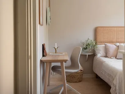 A minimalist bedroom with wooden furniture, a woven headboard bed, and a small wooden desk with a chair, a candle holder, and