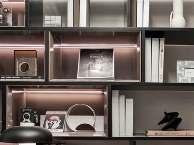 A modern home office with black furniture and white walls, featuring a desk, shelves with books, a desk lamp, and decorative