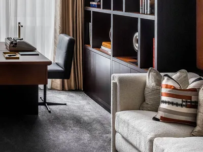 A modern home office featuring a desk, chair, bookshelf, and sofa with cushions.