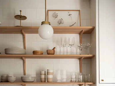 Modern kitchen with open shelving made of wood, containing ceramic and glassware, and a stainless steel sink with brass fixtu