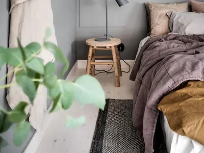 A minimalist bedroom with light grey walls, a wooden stool as a bedside table, and neutral bedding and textiles.