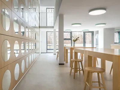 現代極簡餐廳室內，搭配木質餐桌與吧台椅、圓形鏡面以及大面窗戶。