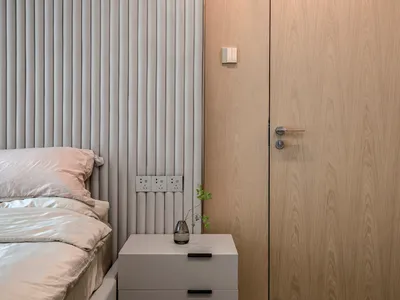 Minimalist bedroom with a wooden wall and fabric headboard, featuring a bedside table with a vase.