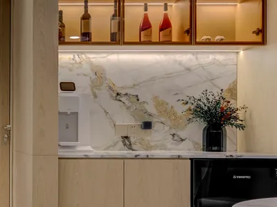 A modern kitchen featuring a marble backsplash and countertop. Includes a white water dispenser and a black microwave.