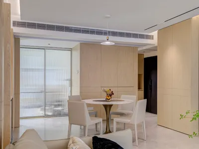 Modern kitchen interior with wooden cabinets, white marble countertop, and white chairs around a round table.