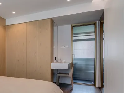 A minimalist bedroom featuring wooden furniture and glass doors, with a wooden bed and a glass-walled closet.