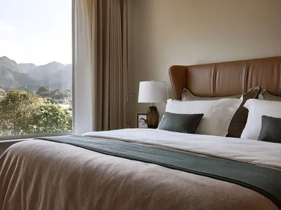 A modern minimalist bedroom with a white bed, leather headboard, and cotton bedding, featuring floor-to-ceiling curtains and