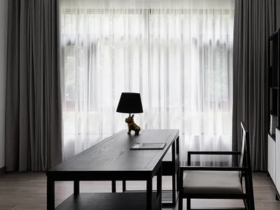 A modern home office with a black desk, white curtains, and a minimalist design.