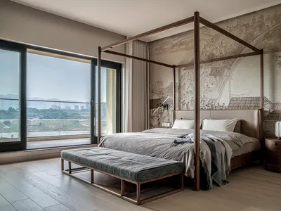 A minimalist bedroom with a wooden frame bed and a large window overlooking a scenic landscape.