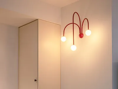 A minimalist home office featuring a sleek, black floating desk and a white wardrobe with a red pendant light on the wall. Th