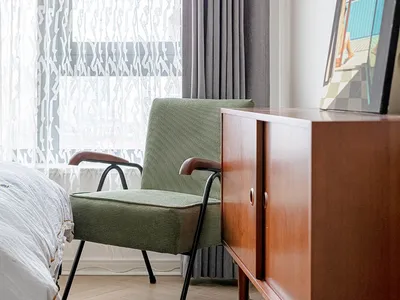 A modern bedroom with a green accent chair and fabric curtains by the window.