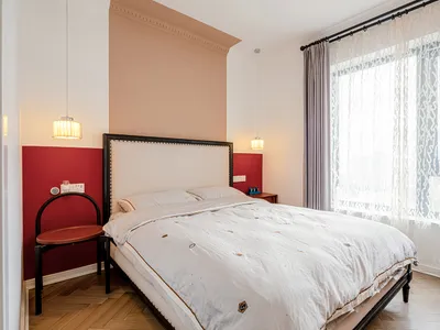 A minimalist bedroom with a white bed, pendant lights, red accent wall, and large window with sheer curtains.