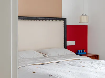 A minimalist bedroom featuring a white fabric headboard with decorative buttons, white bedding, and a red paneled backdrop.