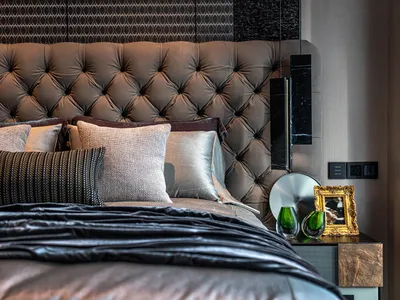 Modern bedroom with a leather headboard, decorative pillows, and green vases on the nightstand.