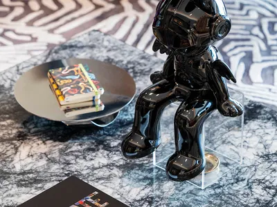 A shiny black metallic statue of a rabbit sitting on a glass table with a red textured chair in the background.