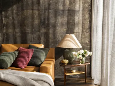 A cozy living room featuring a brown leather sofa with green and red throw pillows, a wooden side table with a ceramic lamp a