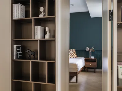 Modern bedroom with wooden shelving unit, white bedding, and dark green accent wall.