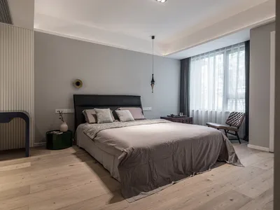 A minimalist bedroom with light wood flooring, a gray bed, and a black headboard.