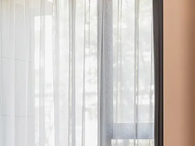 A modern bedroom featuring a leather upholstered chaise lounge under transparent curtains.