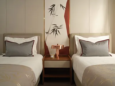 Modern minimalist bedroom with fabric bedding, wood headboards, and a metal desk lamp.