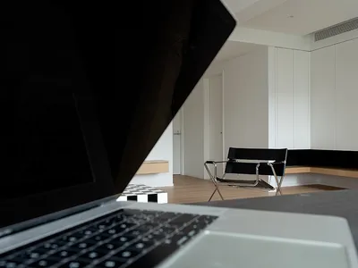 A minimalist home office setup featuring a sleek, modern desk and chair in a well-lit, white room with wooden flooring.