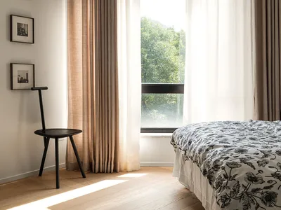 A minimalist bedroom featuring linen curtains, wooden furniture, and glass windows.