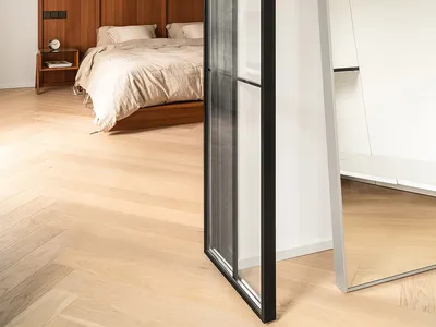 Modern minimalist bedroom featuring wooden walls, a glass closet, and a bed with neutral bedding.