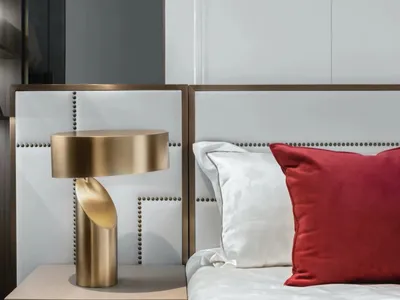 A modern bedroom with a white leather headboard adorned with gold accents and a red decorative pillow, featuring an arc lamp