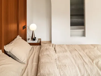 A bed with beige linens and a wooden headboard in a modern bedroom setting.
