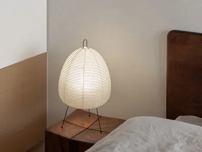 A minimalist bedroom with a wooden nightstand featuring a round lamp with a white shade, positioned next to a bed adorned wit