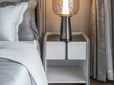 A modern bedroom featuring a glass table lamp and gray bedding with metallic accent.