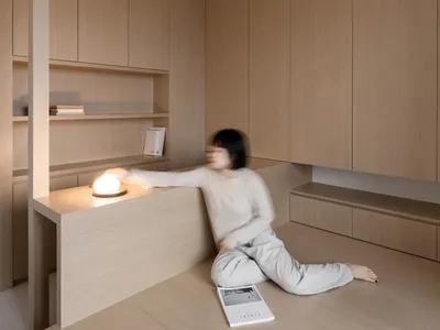 簡約住宅室內使用溫潤木質材料，一人正調整桌燈。