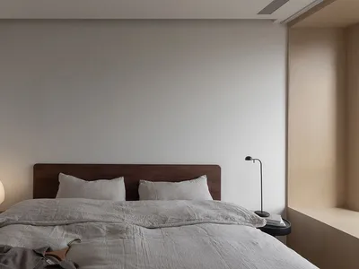 A minimalist bedroom with a bed, nightstand, and lamp, featuring neutral-toned bedding and decor.
