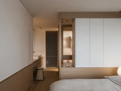 Minimalist bedroom with wooden accents, white walls, and a simple furniture layout.