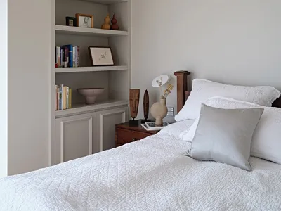 A minimalist bedroom featuring wood accents, fabric bedding, and glass vases, with a bedside table and bookshelf.