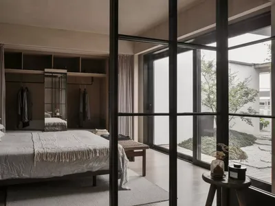 A minimalist bedroom with a wooden bed, white sheets, and a simple wooden side table.