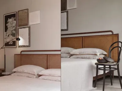 A minimalist bedroom featuring a bed with a wicker headboard, accompanied by a chair with a bowl and fruit.
