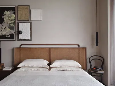 Minimalist bedroom with a wooden rattan headboard, white bedding, and a hanging black lamp.