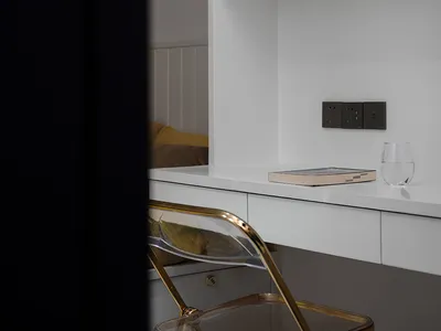 A modern home office with a clear folding chair, matte white wall, and minimalist decor.