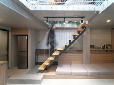 A modern living room featuring industrial design elements like concrete walls, wooden furniture, and metal stairs.