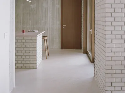 A modern minimalist kitchen with concrete walls, a wooden countertop, and a wooden stool.
