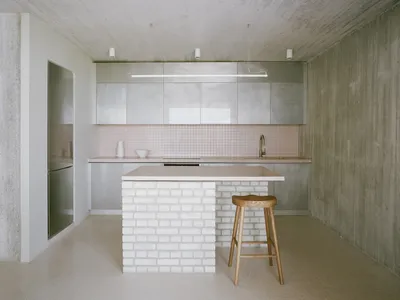 A modern minimalist kitchen features a concrete countertop and white brick island.