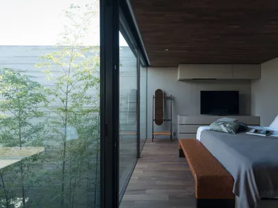 Modern minimalist bedroom with glass walls and wooden floor.