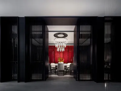 Modern dining room featuring black metallic windows and a red accent wall with a sophisticated chandelier hanging above the d